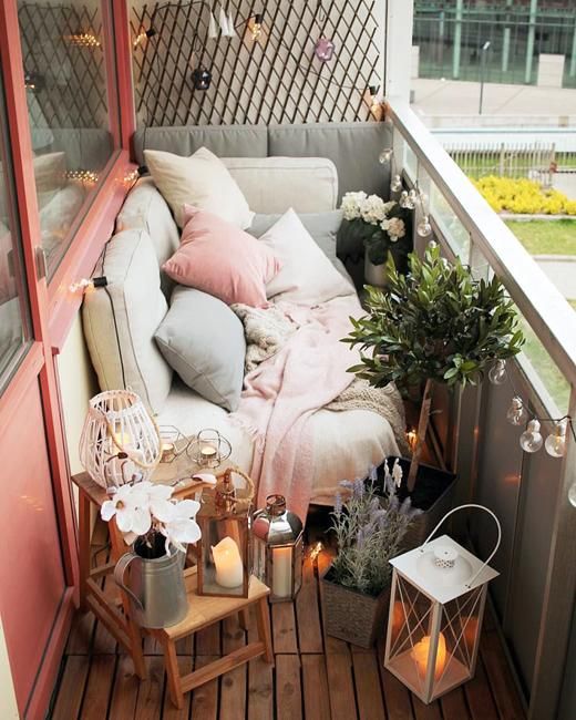 a tiny narrow balcony with pastel textiles and pillows, potted greenery and blooms, candle lanterns and wooden furniture