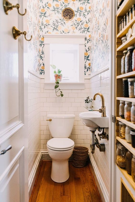 a tiny white powder room with white subway tiles, bright floral wallpaper, a wall-mounted sink and white appliances
