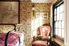 a vintage bedroom with floral wallpaper, a black forged bed, a vintage pink chair and printed textiles