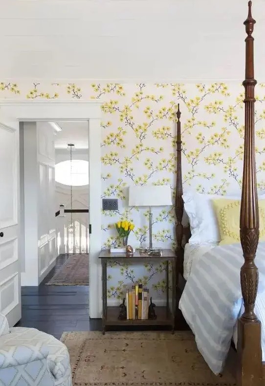 a vintage-inspired bedroom with yellow floral walls, a heavy bed with pillars, a chair and nightstands plus blooms