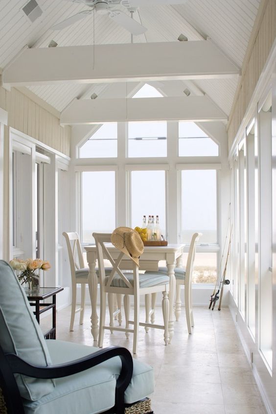 A vintage inspired coastal sunroom with white and black vintage furniture, ligth blue upholstery, chic sea views