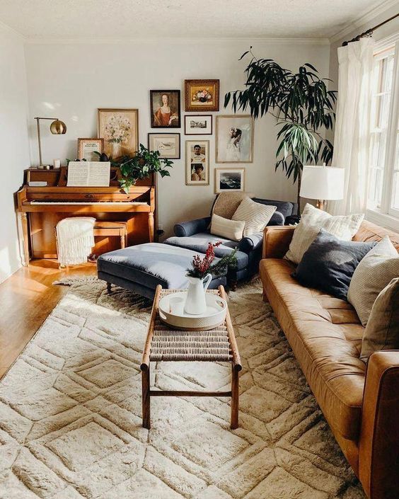 A warm colored living room with an maber sofa, a woden coffee table, a geometric printed rug, a large lounger, a gallery wall and a potted tree