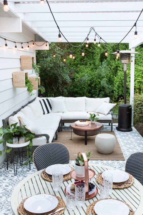 A welcoming terrace with an L shaped bench, a jute rug, a copper table and some greenery on the wall