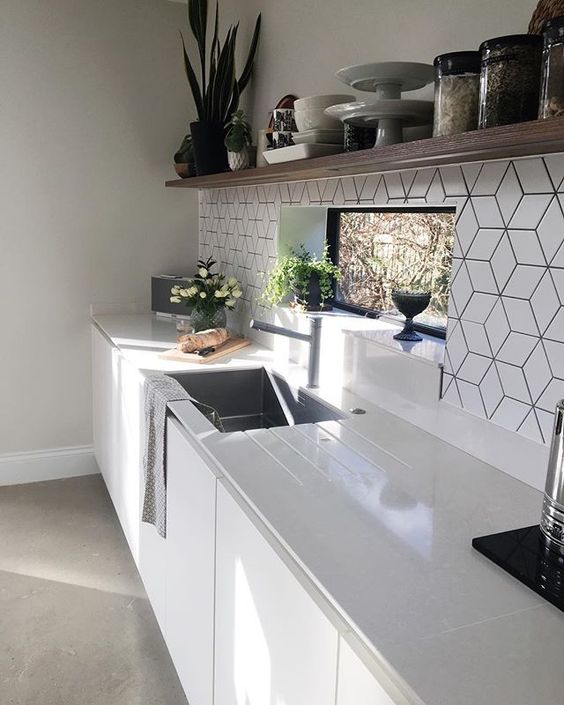 a white Scandinavian kitchen with white countertops, an open shelf for storage and a white geo tile backsplash plus potted plants