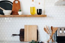 a white Scandinavian kitchen with white hexagon tiles on the backsplash, a wooden shelf and brass handles is all cool