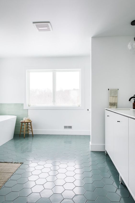 an airy and serene bathroom with blue hex tiles on the floor and a mint backsplash, white furniture and white appliances