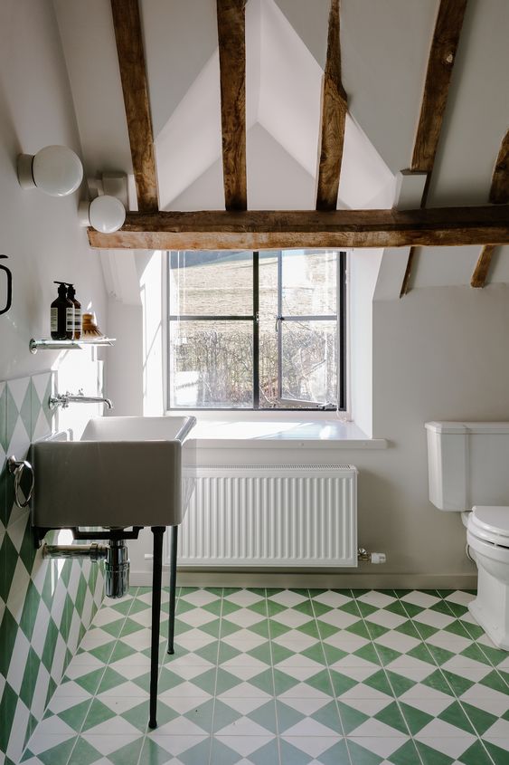 An attic farmhouse bathroom with white and green geo tiles, a free standing sink and white appliances and wooden beams