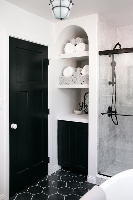 An eye catchy bathroom with grey marble and black hex tiles, white appliances and textiles and black fixtures for a more modern feel