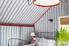an eye-catchy coastal guest bedroom with striped walls and a ceiling, a striped loveseat, a bed with neutral bedding and a catchy lamp