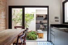 an indoor-outdoor kitchen with sleek grey cabinets and black countertops, a blue and navy geo tile floor and a dining zone with wooden furniture