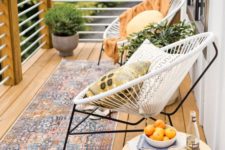 an inviting summer balcony with a boho rug, some round chairs, a table and potted greenery plus pillows