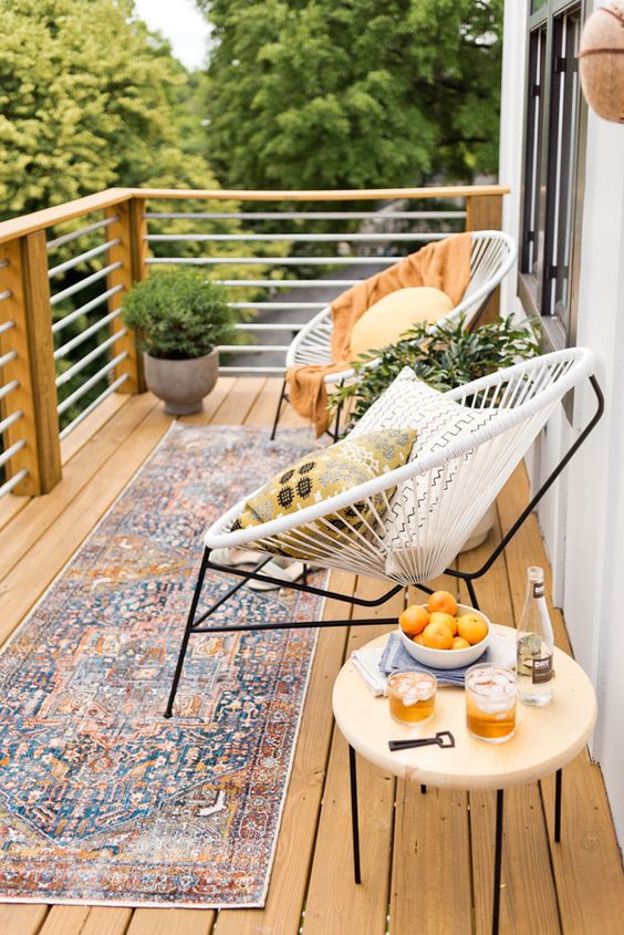 an inviting summer balcony with a boho rug, some round chairs, a table and potted greenery plus pillows