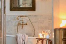 a Provence bathroom with marble tiles, a clawfoot bathtub, a vintage mirror, crystal lamps and candles and vintage fixtures