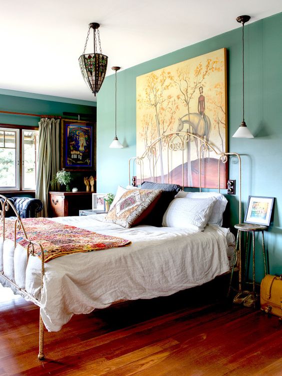 a bold and whimsy vintage bedroom with green walls, a metal bed, colorful bedding, bold artworks and a stained glass chandelier