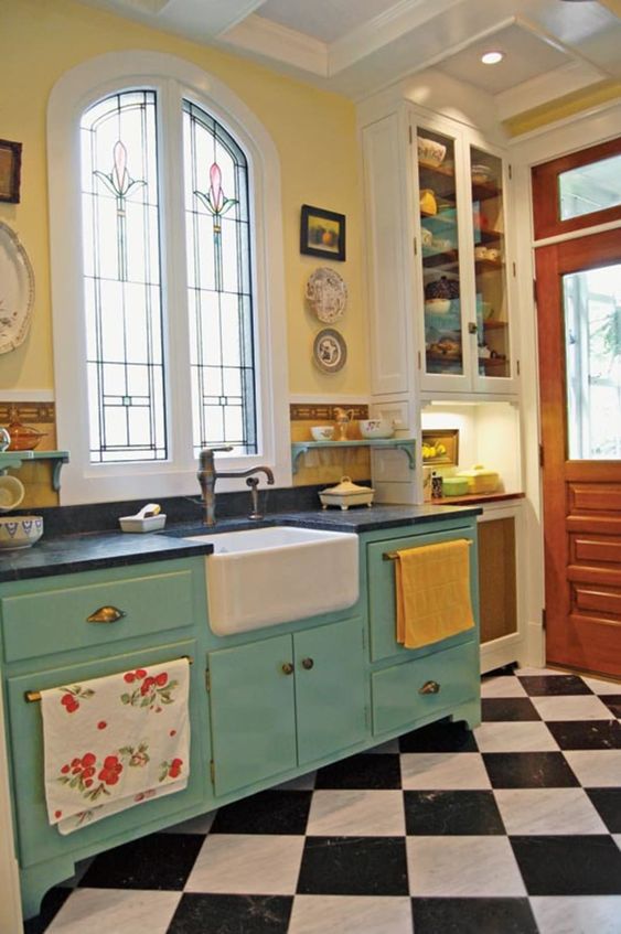 a bright retro kitchen with a checked floor, yellow walls, blue cabinetry, black countertops, vintage faucets and bright textiles