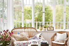 a bright vintage sunroom with a colorful rug, wicker furniture and floral pillows, a potted plant and a mini table