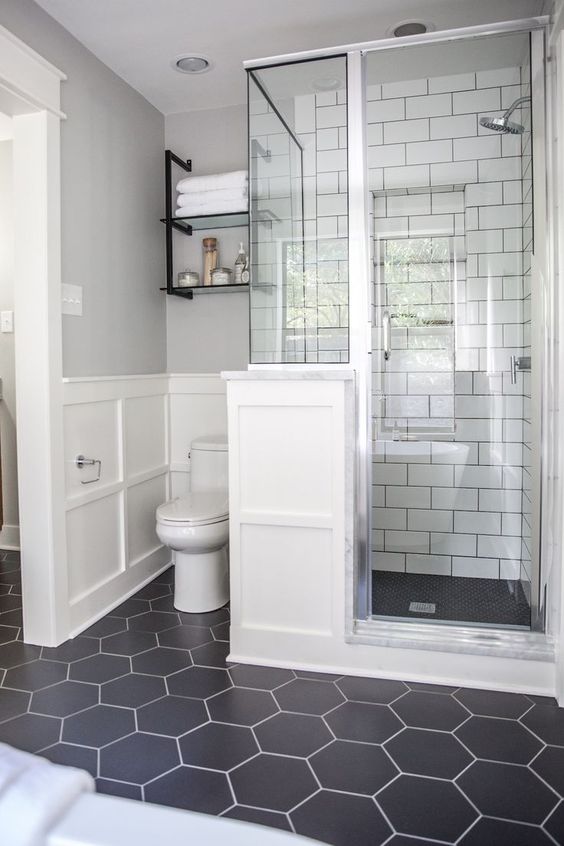 a chic bathroom with a black hex tiles floor, white subway tiles in the shower space and white paneling on the wall