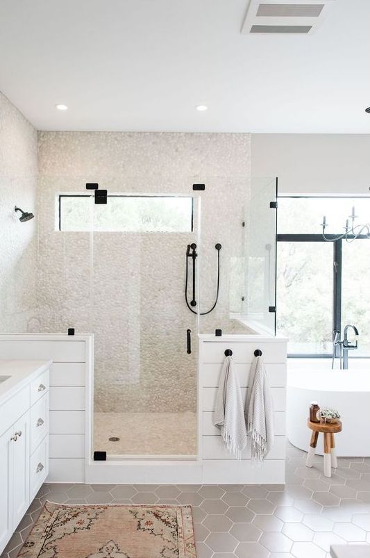 a chic neutral bathroom with grey hex tiles on the floor, faux pebbles in the shower space and planked pony walls and a large window