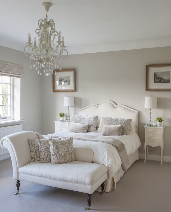 a chic neutral vintage bedroom with dove grey walls, creamy furniture, a crystal chandelier and printed textiles