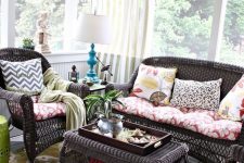 a chic vintage sunroom with dark rattan furniture, colorful textiles, a bright artwork and a blue table lamp