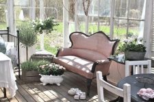 a chic vintage sunroom with neutral forged and wooden furniture, a pink sofa, potted blooms and much sunlight