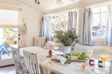 a chic vintage to shabby chic sunroom with white shabby furniture, striped curtains, greenery and a rustic lamp