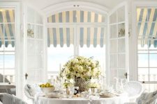 a classic vintage sunroom done in all-neutrals, with a white wicker furniture set, potted blooms and neutral textiles