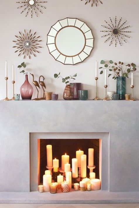 a concrete fireplace with pillar candles in candle holders and mercury glass votives plus colored glass vases on the mantel
