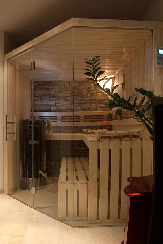 a cozy tine home sauna with wooden benches, a stone accent wall and some intimate light plus a glass wall