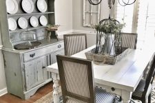 a greyish dining room with a whitewashed buffet, a white table, striped chairs and a vintage chandelier