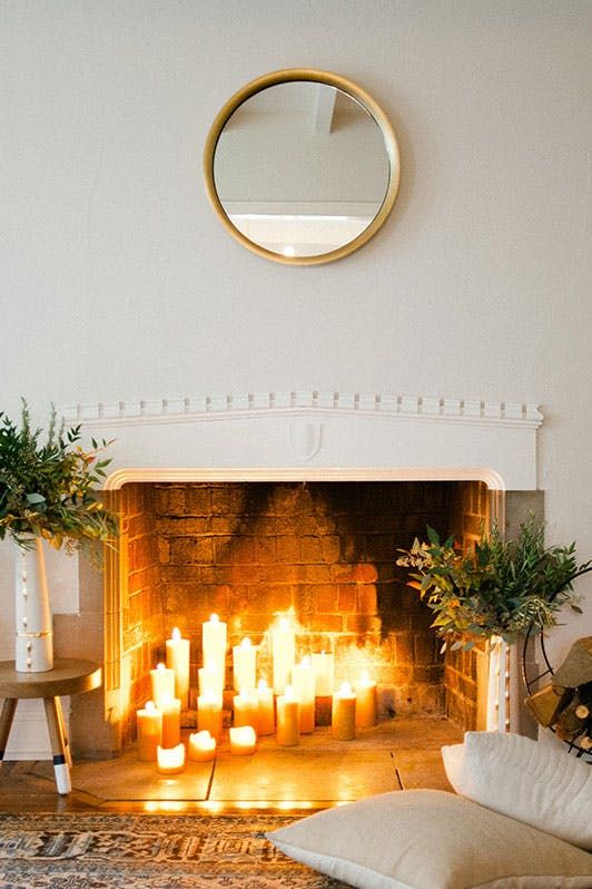 a hygge fireplace with lots of candles and greenery arrangements in beautiful vases for a natural feel