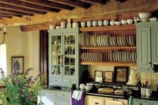 a lovely vintage kitchen with blue cabinets, a vintage hearth, open shelves for plates, wooden beams and a wooden dining set