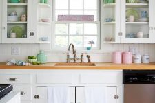 a lovely vintage kitchen with white cabinets, a white beadboard kitchen island,pink, blue and green accessories and neutral linens