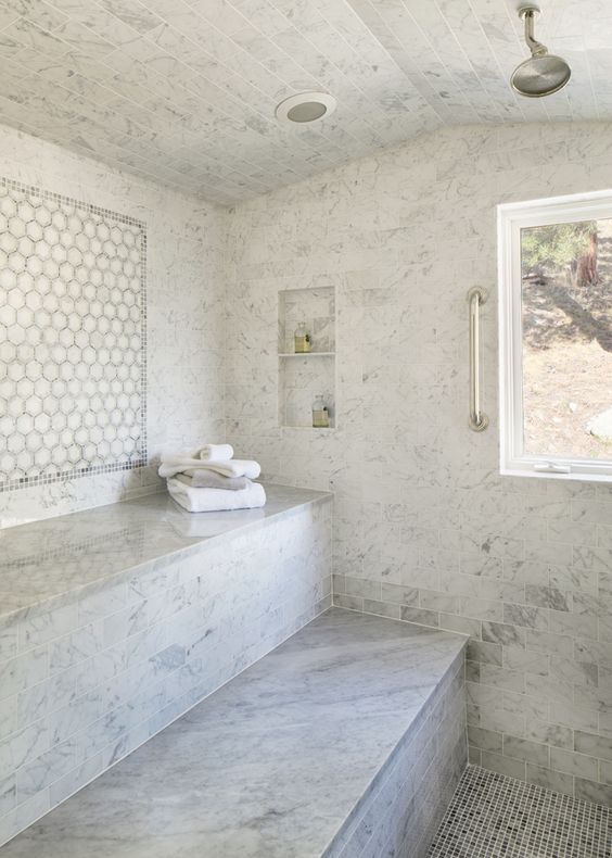 a luxurious white marble tile steam room with two long benches, niches and a window to enjoy the views