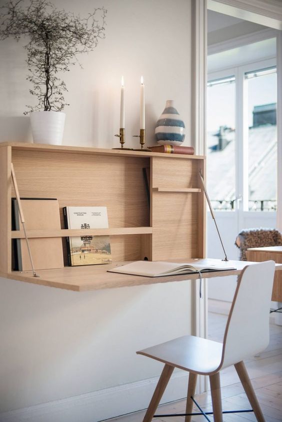 A minimalist wall mounted desk with storage space inside, some candles and a desk surface that can be hidden
