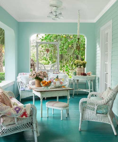 a minty and turquoise vintage sunroom with white wicker furniture, floral textiles, potted blooms and greenery