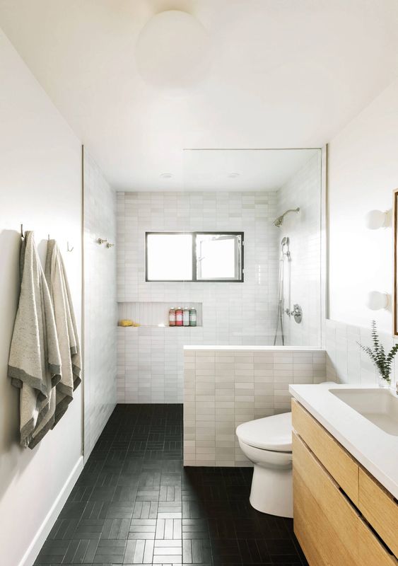 A modern bathroom with marble skinny tiles and black ones on the floor, a floating wooden vanity, a built in niche for storage