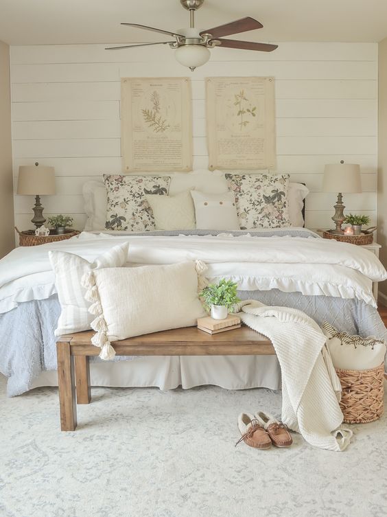 a neutral and pastel Provence bedroom with a shiplap accent wall, a bed with lovely bedding, white nightstands and table lamps, greenery and botanical prints