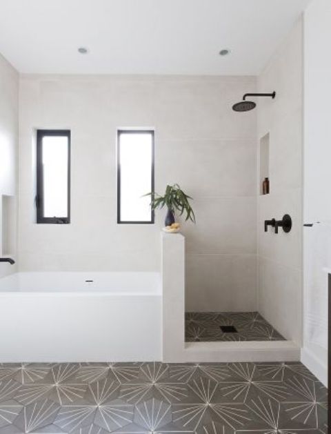 a neutral bathroom with mosaic tiles on the floor and neutral ones on the walls, a shower space with a pony wall that separates a shower and a bathtub