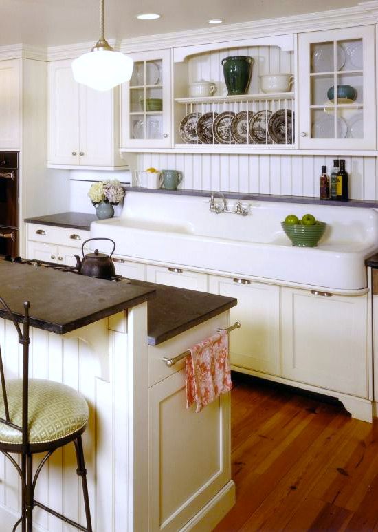 a neutral kitchen with white cabinets and a kitchen island, dark stained countertops, glass and usual cabinets and printed decor