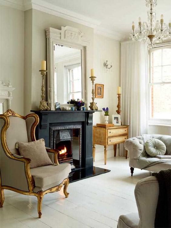a neutral living room with a black fireplace, chic seating furniture, a stained dresser, a large mirror and a chic chandelier