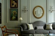 a neutral living room with elegant and refined paneling, a grey sofa, neutral chairs, a glass coffee table and some lovely artwork