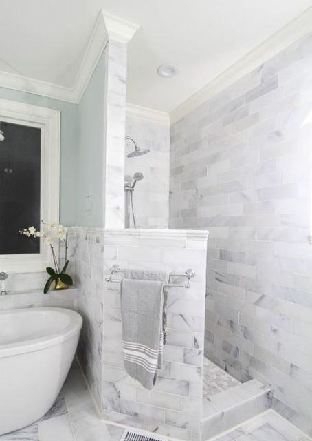 a neutral marble bathroom with a shower space with a pony wall, a bathtib and blue walls is very refined