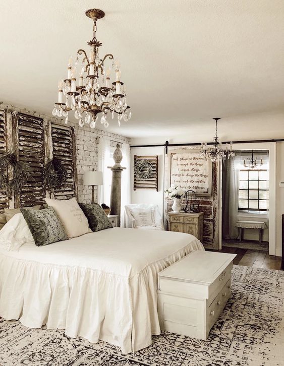 a neutral vintage bedroom with brick walls, shutters, a crystal chandelier and chic furniture plus artworks
