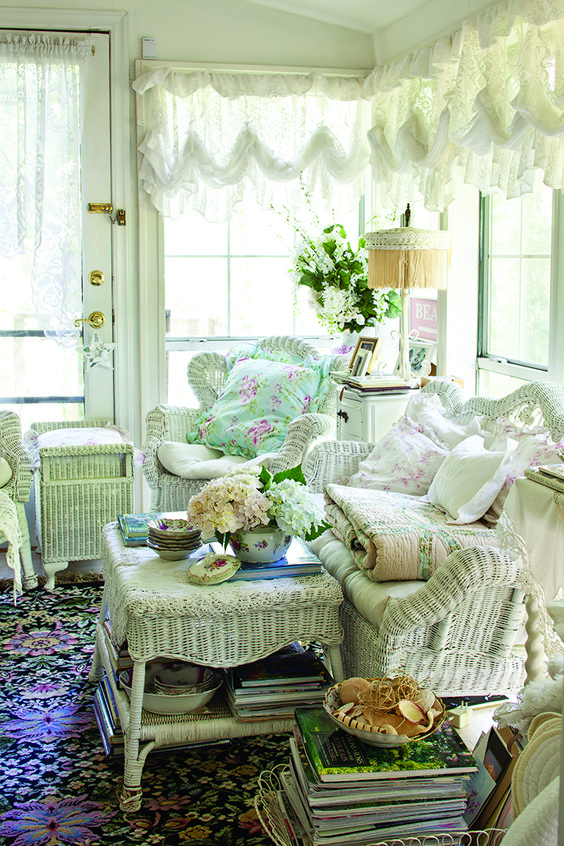 a neutral vintage sunroom with white wicker furniture, tulle ruffle curtains, floral textiles and a colorful rug