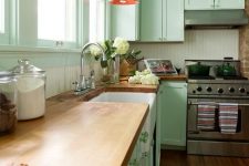 a pretty mint green kitchen with a white beadboard backsplash, butcherblock countertops, red pendant lamps and green knobs