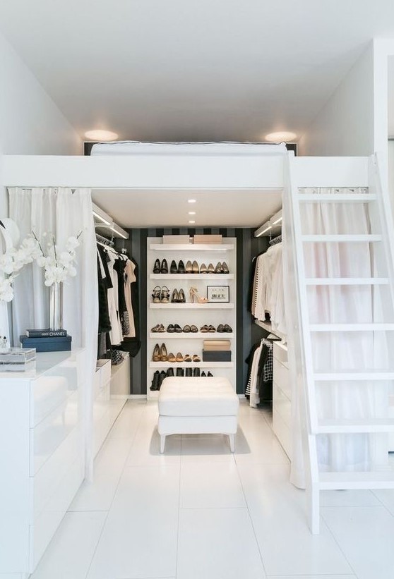 A refined and chic black and white space with a walk in closet, a ladder and a loft sleeping space, sleek white furniture is amazing