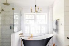 a refined farmhouse bathroom clad with hex and subway tiles, with a vintage bathtub, a stool with a plant and a vintage chandelier