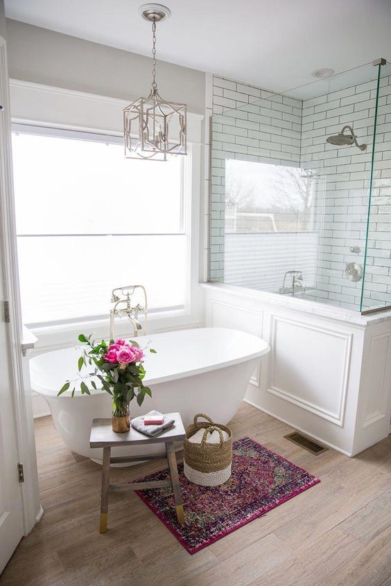 a refined farmhouse bathroom with a shower space with half walls, a small tub, a wooden stool and a chic chandelier