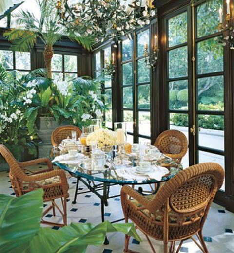a refined vintage sunroom with a glass table and wicker chairs, a crystal chandelier with blooms and potted blooms and greenery